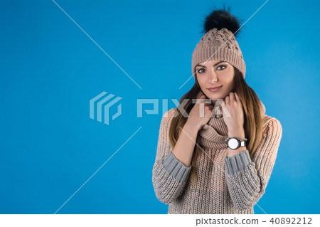 Girl in a warm sweater, scarf and hat on a blue background Girl in a warm sweater, scarf and hat on a blue background 40892212