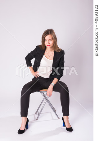 Full length studio portrait of young business woman in black suit, high heel shoes, sitting in chair Full length studio portrait of young business woman in black suit, high heel shoes, sitting in chair 40893122