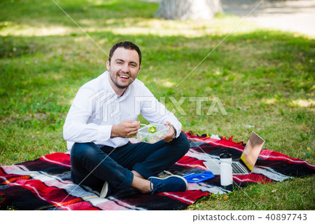 young business man enjoying food which he brought in a lunch box from home. Lunchtime at the park young business man enjoying food which he brought in a lunch box from home. Lunchtime at the park 40897743