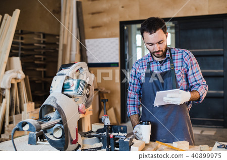 Carpenter taking a coffee break holding notebook in front of circular saw at his workshop 40899975