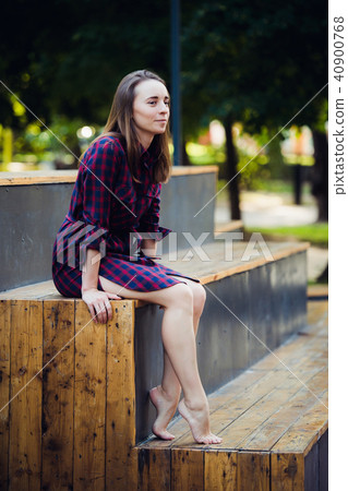 Girl wearing checkered dress sitting down in skatepark looking at camera. Girl wearing checkered dress sitting down in skatepark looking at camera. 40900768