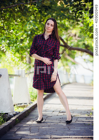 Beautiful, pretty woman in casual checkered dress walking at park outdoors. Street fashion style. 40900949