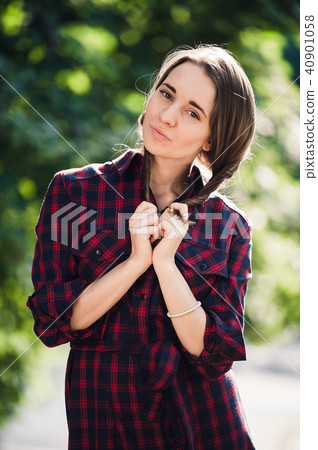 Cute teenage girl in casual dress playing with her braids, looking at camera and smiling, standing 40901058