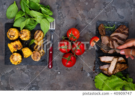 female hand holds a fork with slice tomato on the background fresh three types of grilled steak on 40909747