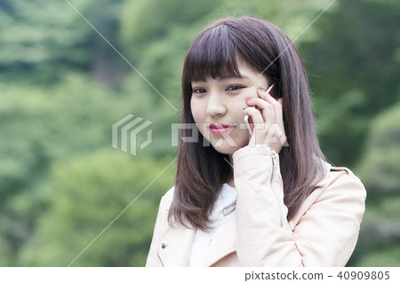 一位年輕的女士,她使用智能手機與新鮮的綠色公園交談 一位年輕的女士,她使用智能手機與新鮮的綠色公園交談 40909805
