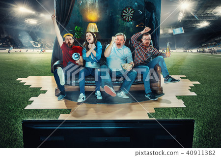 Soccer football fans sitting on the sofa and watching TV in the middle of a football field. Soccer football fans sitting on the sofa and watching TV in the middle of a football field. 40911382
