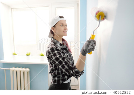 Girl painter, designer and worker paints a roller and brush the wall. Smiling, working with pleasure Girl painter, designer and worker paints a roller and brush the wall. Smiling, working with pleasure 40912832