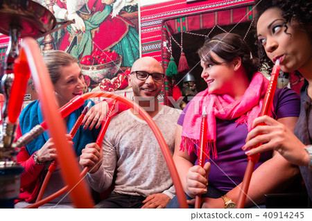 Women and man enjoying recreational shisha in hookah lounge Women and man enjoying recreational shisha in hookah lounge 40914245