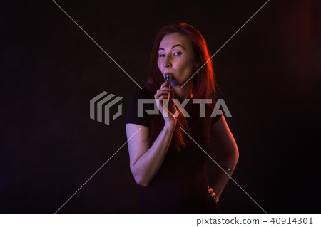 young woman smoking electronic cigarette on dark background 40914301