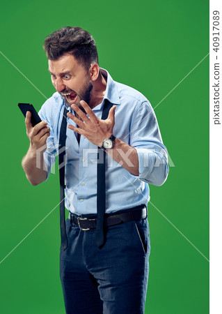 The young emotional angry man screaming on green studio background 40917089