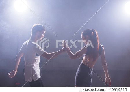 Skillful dancers performing in the dark room under the concert light and smoke. Sensual couple Skillful dancers performing in the dark room under the concert light and smoke. Sensual couple 40919215