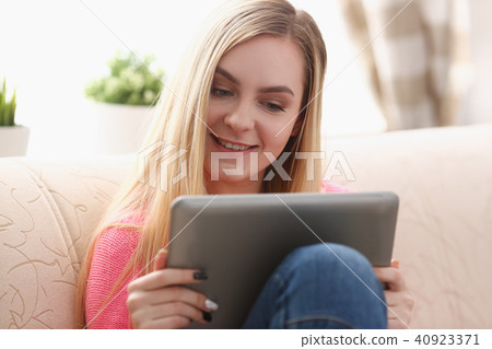 young beautiful blond woman sit on the sofa in livingroom hold tablet in arms 40923371