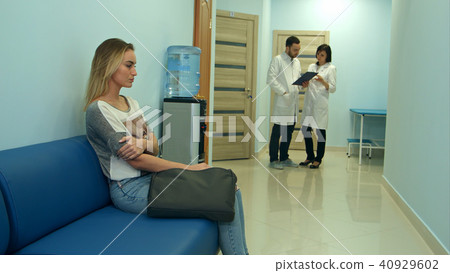 Female patient waiting in hospital hall while two doctors consulting 40929602