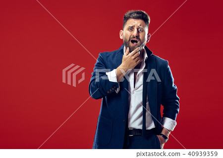 Beautiful man looking suprised and bewildered isolated on red 40939359