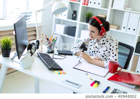 Beautiful young girl is sitting in headphones and with a microphone at the desk in the office. 40948002