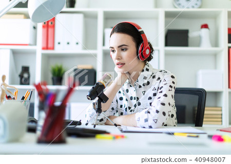 Beautiful young girl sitting in headphones and with microphone at table in office and talking. 40948007