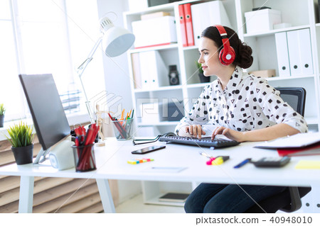 Beautiful young girl sitting in headphones at desk in office and typing on keyboard. 40948010