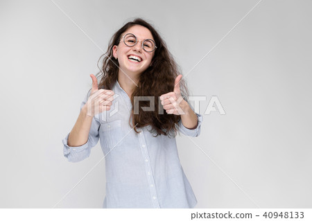 Portrait of a young girl in glasses. Beautiful young girl on a gray background. The girl shows the Portrait of a young girl in glasses. Beautiful young girl on a gray background. The girl shows the 40948133