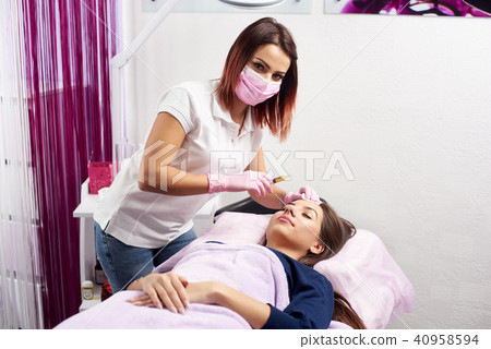 Cosmetologist is looking in the camera while giving facial treatment with a syringe to a client of a 40958594