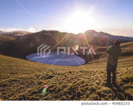 一名穿著綠色外套的男性登山客, 站在高處拍攝嘉明湖的日出, 嘉明湖位於台灣台東縣 40960233