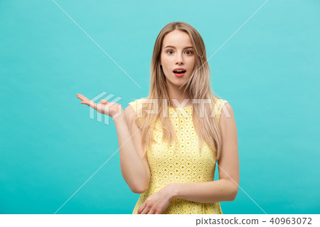 Woman surprise showing product. Beautiful girl with curly hairstyle pointing to the side. Presenting 40963072