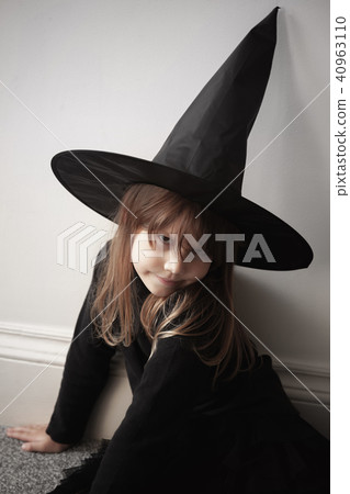 Girl in black witch costume sitting near wall Girl in black witch costume sitting near wall 40963110
