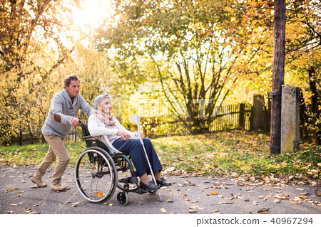 Senior man and woman in wheelchair in autumn nature. Senior man and woman in wheelchair in autumn nature. 40967294