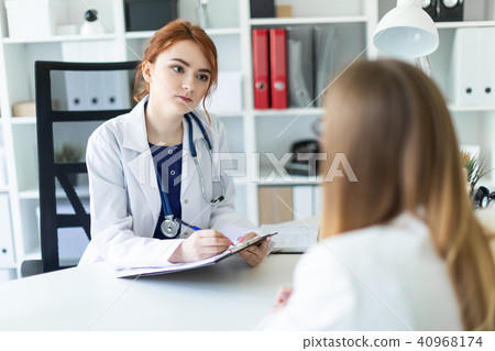 A beautiful young girl in a white robe is sitting at the desk in the office and communicating with A beautiful young girl in a white robe is sitting at the desk in the office and communicating with 40968174
