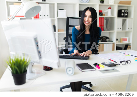A young girl is sitting at the office at the table and typing text on the keyboard. A young girl is sitting at the office at the table and typing text on the keyboard. 40968209
