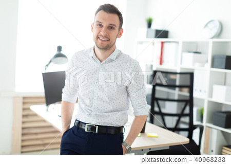A young man stands leaning on a table in the office. A young man stands leaning on a table in the office. 40968288