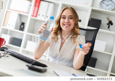 A beautiful young girl sits in the office and holds a water bottle in her hand. 40968353