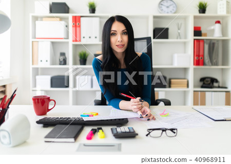 A young girl sits in the office at the table, holds a pen in her hand and fills out the documents. A young girl sits in the office at the table, holds a pen in her hand and fills out the documents. 40968911
