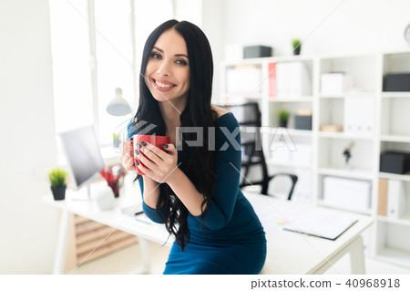 A young girl in the office sat down on the table and was holding a red cup in her hands. A young girl in the office sat down on the table and was holding a red cup in her hands. 40968918