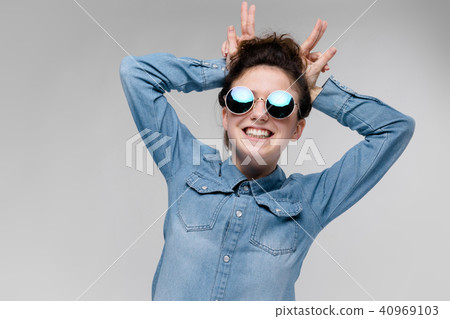Young brunette girl in round glasses. Hairs are gathered in a bun. The girl made herself a horn. 40969103