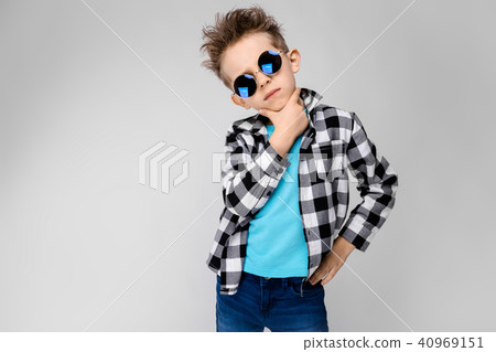A handsome boy in a plaid shirt, blue shirt and jeans stands on a gray background. The boy is A handsome boy in a plaid shirt, blue shirt and jeans stands on a gray background. The boy is 40969151