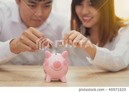 couple putting a coin into a pink piggy bank couple putting a coin into a pink piggy bank 40971820