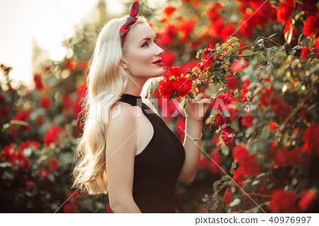 Portrait of beautiful happy blonde girl in bush of red roses 40976997