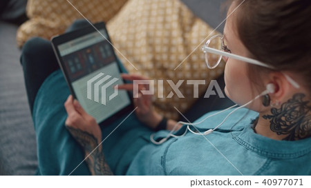 Modern girl with headphones reads an e-book and scrolls screen. Modern girl with headphones reads an e-book and scrolls screen. 40977071