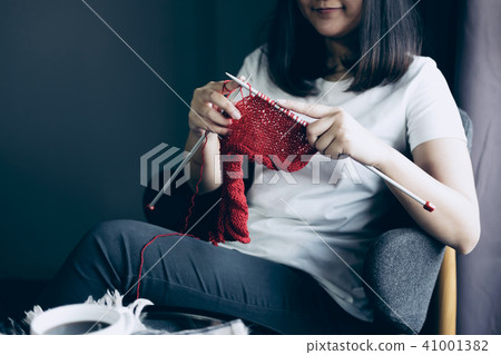Close up shot of young woman hands knitting a red scarf handicra 41001382