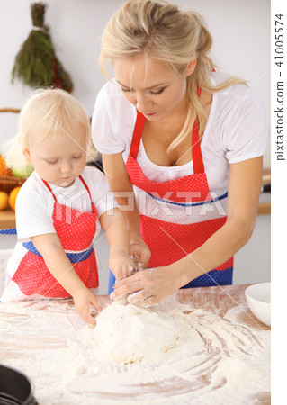Little girl and her blonde mom in red aprons  playing and laughing while kneading the dough in th 41005574
