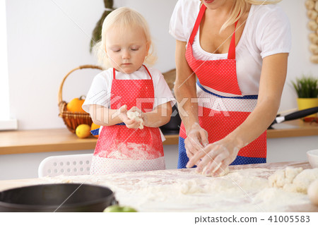 Little girl and her blonde mom in red aprons  playing and laughing while kneading the dough in th 41005583