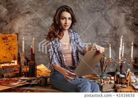The young attractive artist in the course of drawing looks forward at an image with which she paints The young attractive artist in the course of drawing looks forward at an image with which she paints 41016638