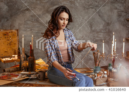 The young attractive artist in the course of drawing estimates a look the done work. She draws oil The young attractive artist in the course of drawing estimates a look the done work. She draws oil 41016640