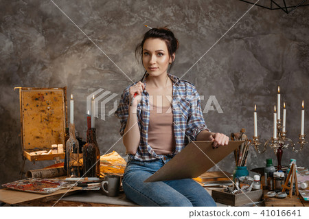 Woman painter sitting on the table, drawing and looking forward. Creative concept. Drawing supplies Woman painter sitting on the table, drawing and looking forward. Creative concept. Drawing supplies 41016641