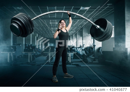 Female athlete with big barbell talking by phone Female athlete with big barbell talking by phone 41040877