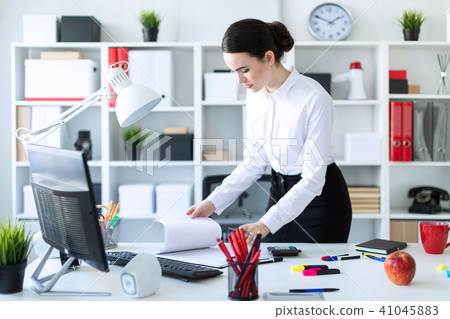 A young girl in the office is standing by the table, holding a pencil in her hand and looking 41045883