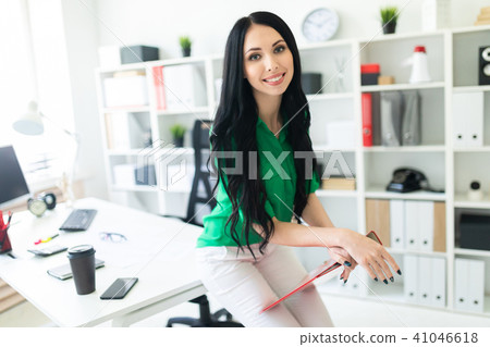 A young girl in the office sat down on the table and was holding a folder with documents. 41046618