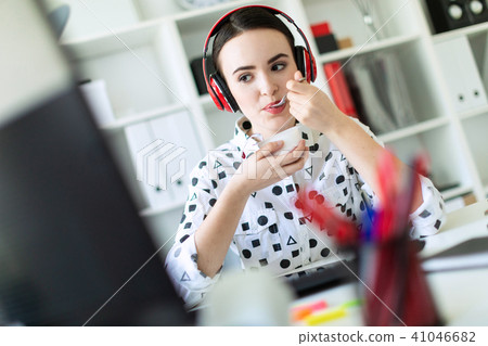 Beautiful young girl sitting in headphones at desk in office, eating yogurt and looking at monitor. 41046682
