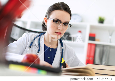 A beautiful young girl in a white robe is sitting at the computer desk with a marker and a book. A 41046685
