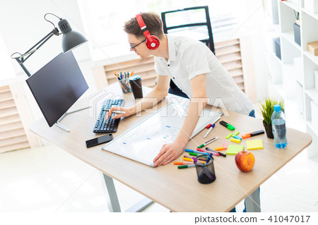 A young man with glasses and headphones stands near a computer desk, holds a marker in his hand and 41047017